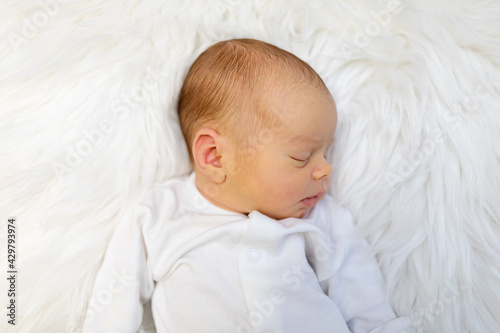 Adorable newborn one week age in white bedroom. Newborn child relaxing in bed. Nursery for young children. Textile and bedding for kids. Family morning at home. Lifestyle concept, real life.