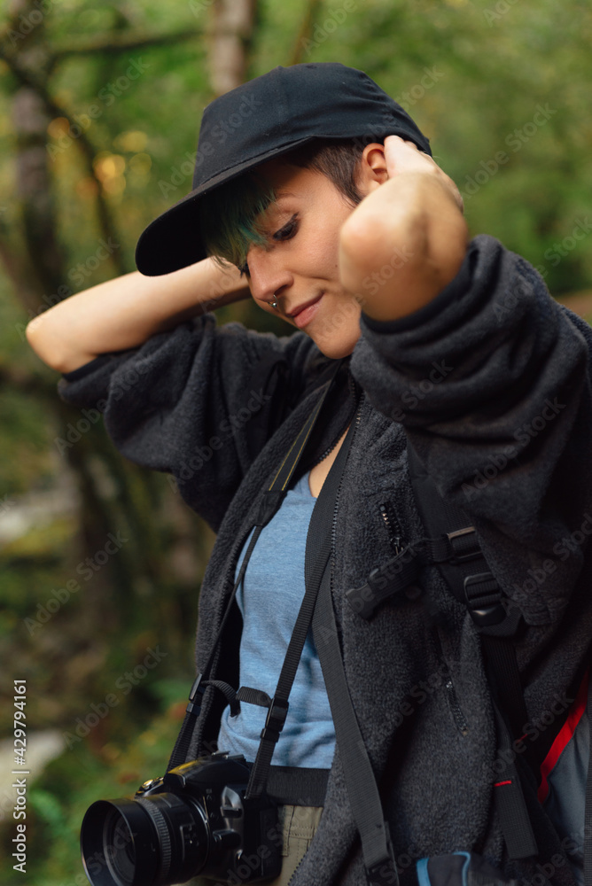 young woman with photo camera posing in the forest. girl with cap enjoying a session of mountain hiking. outdoor activities. nature photographer.