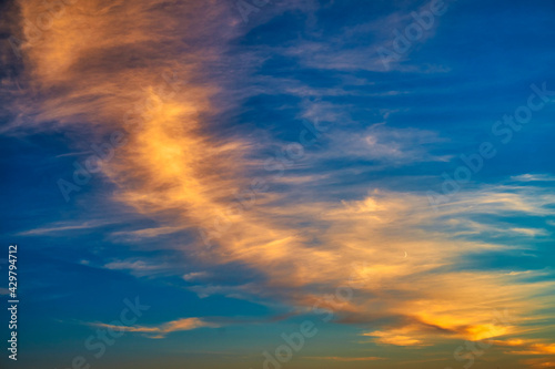 Сolorful cirrus clouds in warm colors from the setting sun against a blue sky.