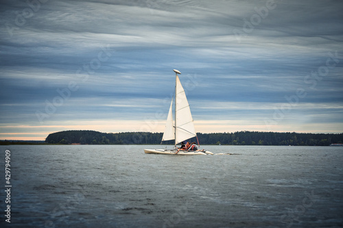 A group of friends ride a small sailing catamaran.