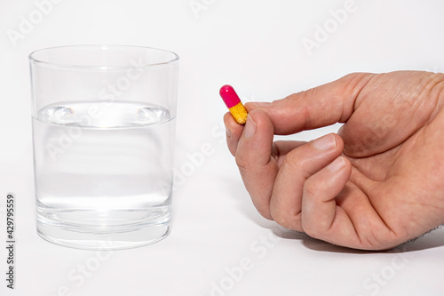 close up of male hands holding pill capsule vitamin supplement with glass of water on white background close up