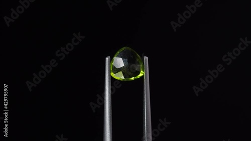 natural peridot gemstone in the tweezer on the background