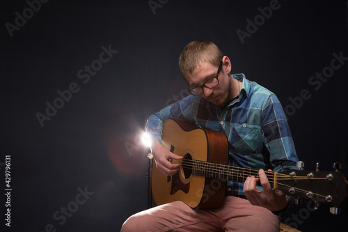 Handsome young musician playing the guitar on dark background