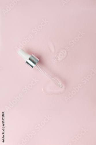 Cosmetic pipette with a drop close up on pink pastel background, vertical. Beautician, cosmetology minimal stylish concept, wellness, skincare, face tune, moisturizing treatment