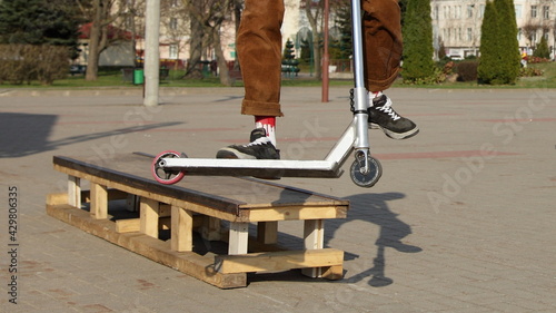 Rider guy on trick kick roller drops from the ramp deck close-up, European city extreme junior people sports outdoor on a Sunny spring day