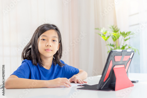 Asian kid girls study online via the internet on a tablet while in the living room at the home, kids and education concepts.