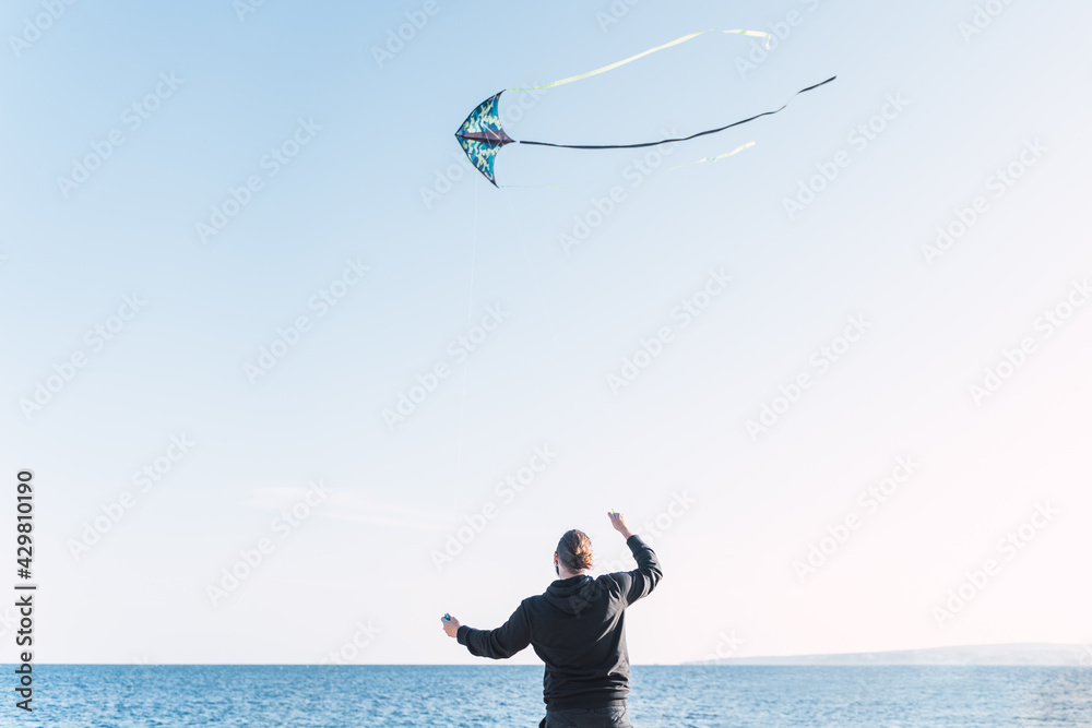 Caucasian man with long hair and beard flying a kite by the sea on a beach in Portals. Palma de Mallorca, Spain (Copyspace)