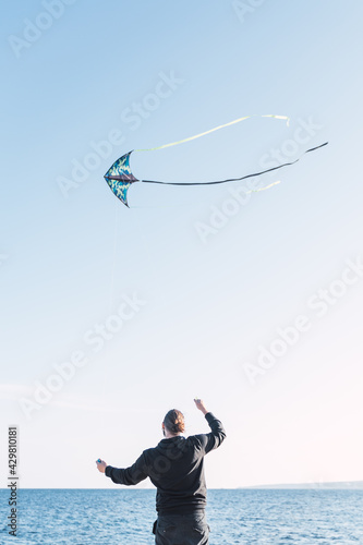 Caucasian man with long hair and beard flying a kite by the sea on a beach in Portals. Palma de Mallorca, Spain (Copyspace)