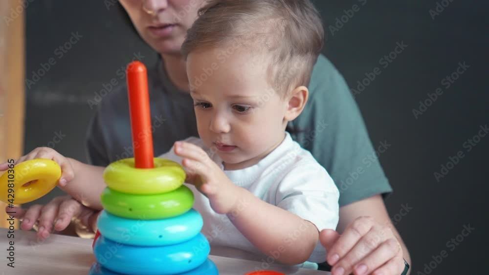 baby collects toy pyramid. mom plays with her son at home happy family. development of fine motor skills in newborn child. happy family mom and baby play pyramid toy. kindergarten preschool education baby collects toy pyramid. mom plays with her son at home happy family. development of fine motor skills in newborn child. happy family mom and baby play pyramid toy. kindergarten preschool education
