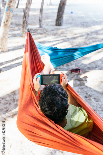 Obraz na płótnie Hispanic man lying in a hammock and playing video games at Palmanova beach. Palma de Mallorca, Spain w salonie