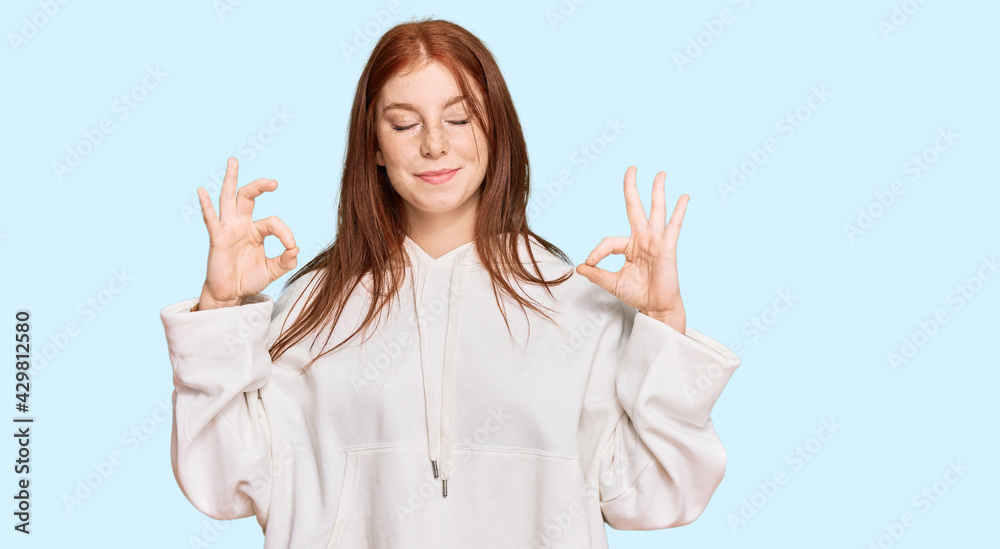 Young read head woman wearing casual sweatshirt relax and smiling with eyes closed doing meditation gesture with fingers. yoga concept. Young read head woman wearing casual sweatshirt relax and smiling with eyes closed doing meditation gesture with fingers. yoga concept.