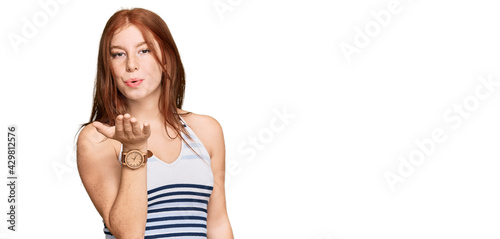 Young read head woman wearing casual clothes looking at the camera blowing a kiss with hand on air being lovely and sexy. love expression.