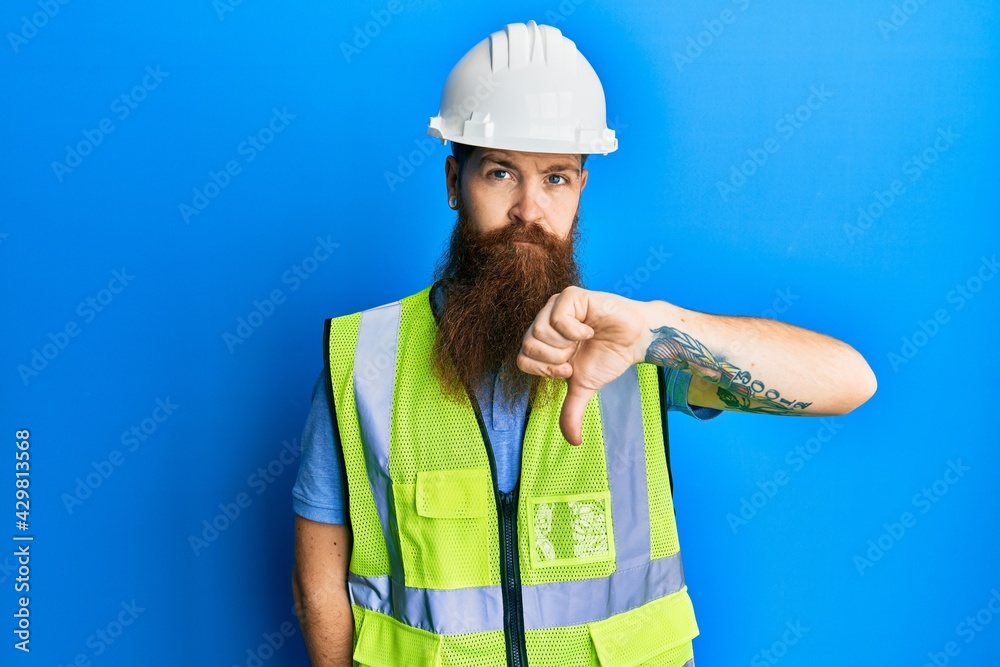 Redhead man with long beard wearing safety helmet and reflective jacket looking unhappy and angry showing rejection and negative with thumbs down gesture. bad expression. Redhead man with long beard wearing safety helmet and reflective jacket looking unhappy and angry showing rejection and negative with thumbs down gesture. bad expression.