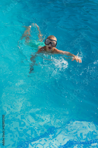 BLOND BOY WITH DIVING GOGGLES IN THE SWIMMING POOL