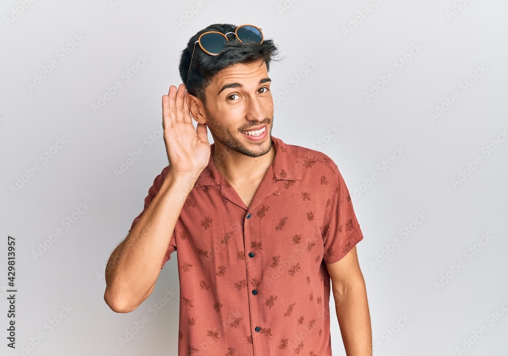 Young handsome man wearing casual summer clothes smiling with hand over ear listening an hearing to rumor or gossip. deafness concept. Young handsome man wearing casual summer clothes smiling with hand over ear listening an hearing to rumor or gossip. deafness concept.