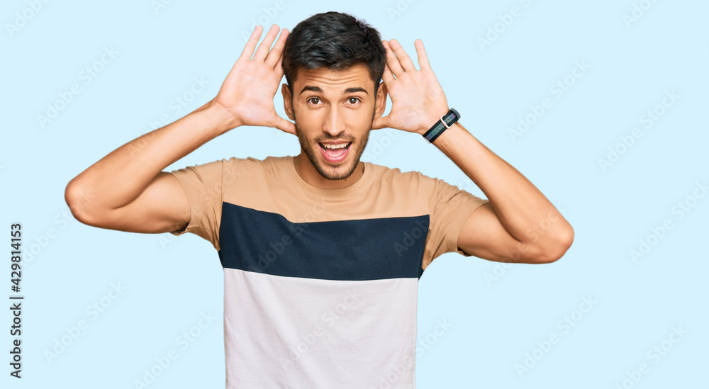 Young handsome man wearing casual clothes smiling cheerful playing peek a boo with hands showing face. surprised and exited Young handsome man wearing casual clothes smiling cheerful playing peek a boo with hands showing face. surprised and exited
