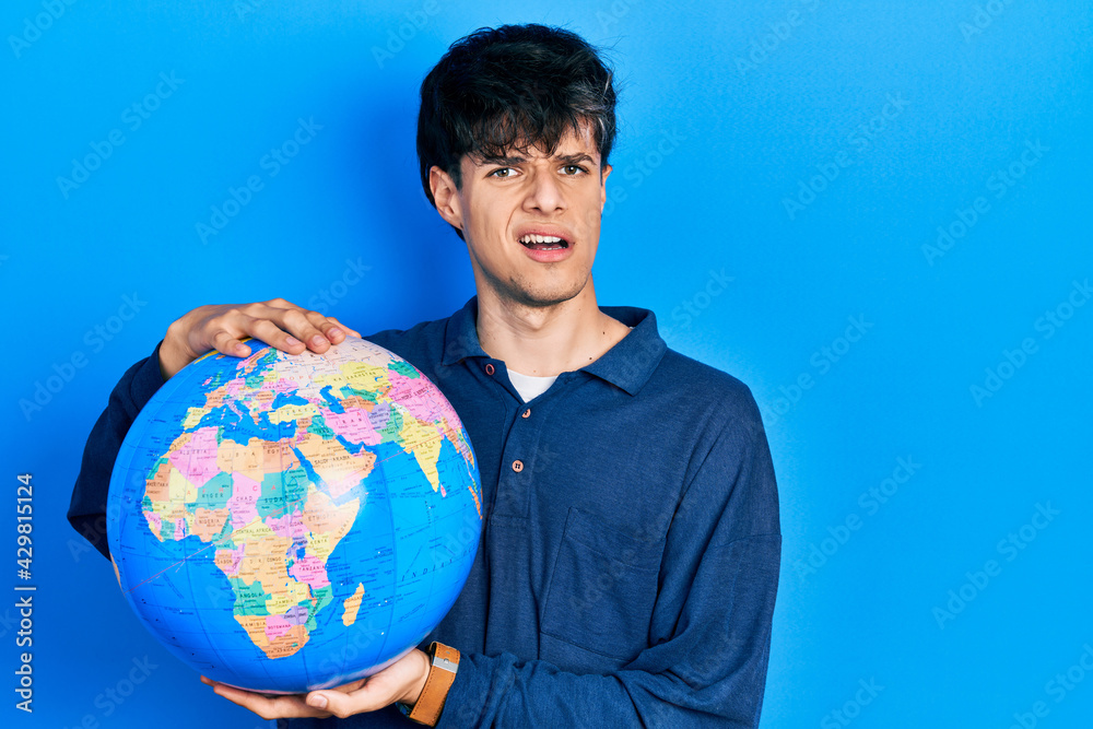 Handsome hipster young man holding world ball clueless and confused expression. doubt concept. Handsome hipster young man holding world ball clueless and confused expression. doubt concept.