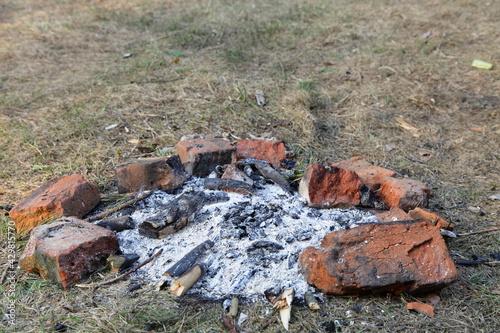 Gray ashes in abandoned fire place red bricks ring on grass close up, outdoors picnic leisure, empty campsite fireplace safety on a spring day, picture with copy space