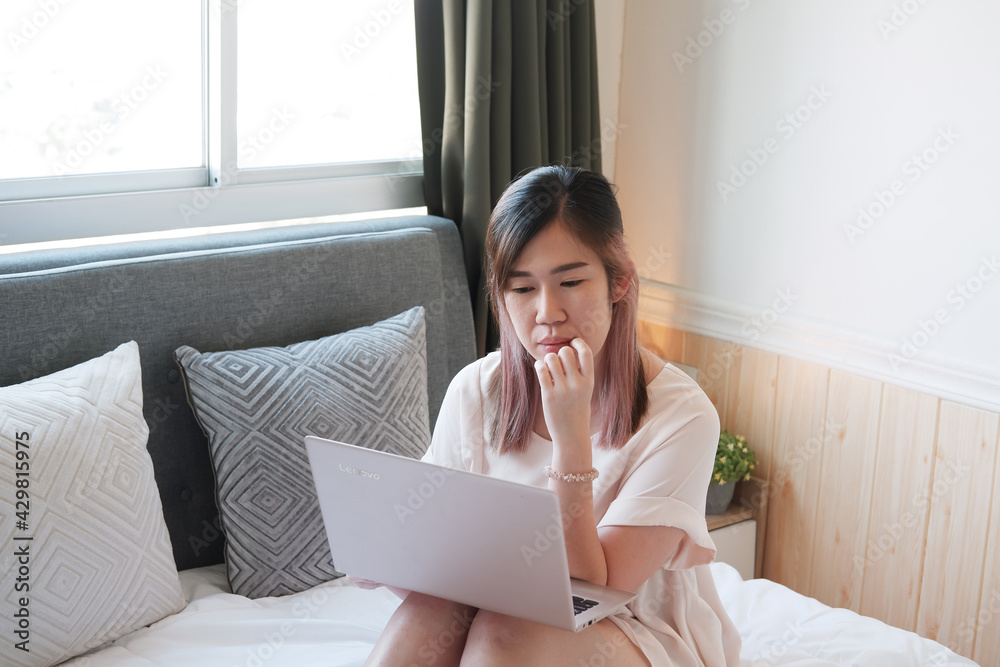 Smiling Young Asian young woman is online working or shopping with laptop in bedroom. She is searching information on internet and work from home. Businesswoman work with technology concept. Smiling Young Asian young woman is online working or shopping with laptop in bedroom. She is searching information on internet and work from home. Businesswoman work with technology concept.