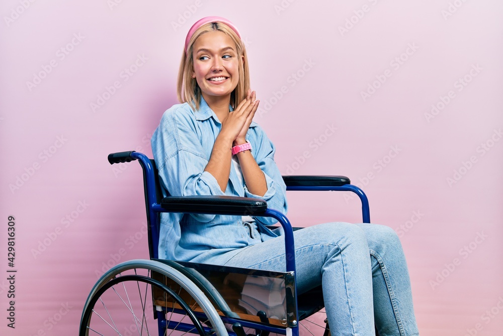 Beautiful blonde woman sitting on wheelchair laughing nervous and excited with hands on chin looking to the side Beautiful blonde woman sitting on wheelchair laughing nervous and excited with hands on chin looking to the side