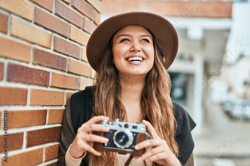 Young hispanic tourist woman smiling happy using vintage camera at the city.