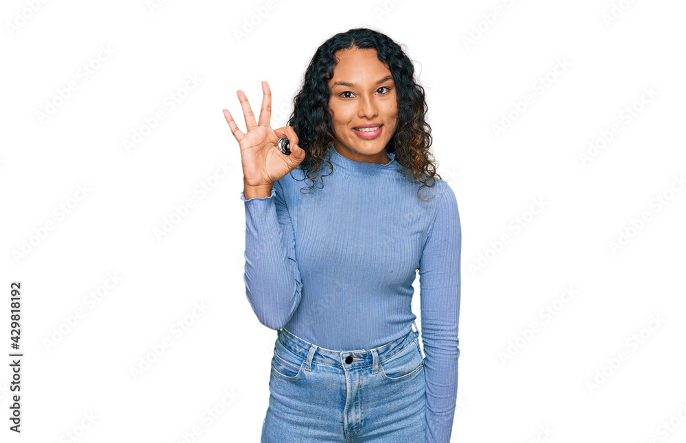Young hispanic woman with curly hair wearing casual clothes smiling positive doing ok sign with hand and fingers. successful expression. Young hispanic woman with curly hair wearing casual clothes smiling positive doing ok sign with hand and fingers. successful expression.