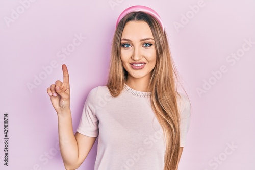 Young blonde girl wearing casual clothes showing and pointing up with finger number one while smiling confident and happy.