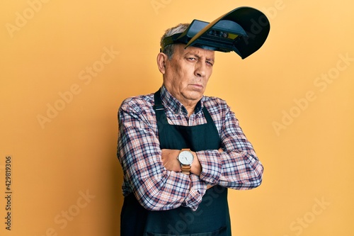 Фотография Handsome senior man with grey hair wearing welding protection mask skeptic and nervous, disapproving expression on face with crossed arms