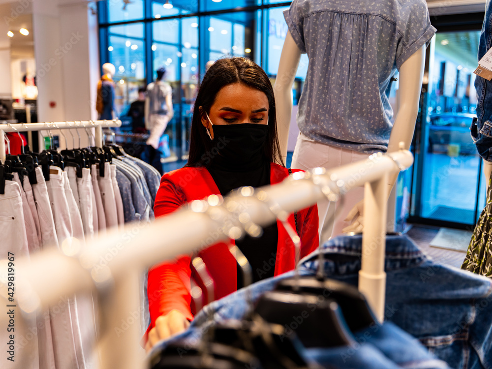 beautiful girl with a protective mask in the clothing store during covid-19 looking for some new clothes to buy