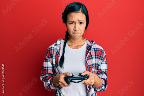 Beautiful hispanic woman playing video game holding controller skeptic and nervous, frowning upset because of problem. negative person.