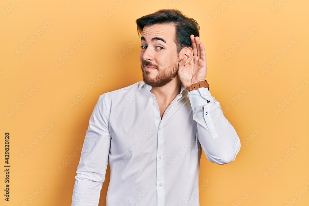 Handsome caucasian man with beard wearing business white shirt smiling with hand over ear listening and hearing to rumor or gossip. deafness concept. Handsome caucasian man with beard wearing business white shirt smiling with hand over ear listening and hearing to rumor or gossip. deafness concept.