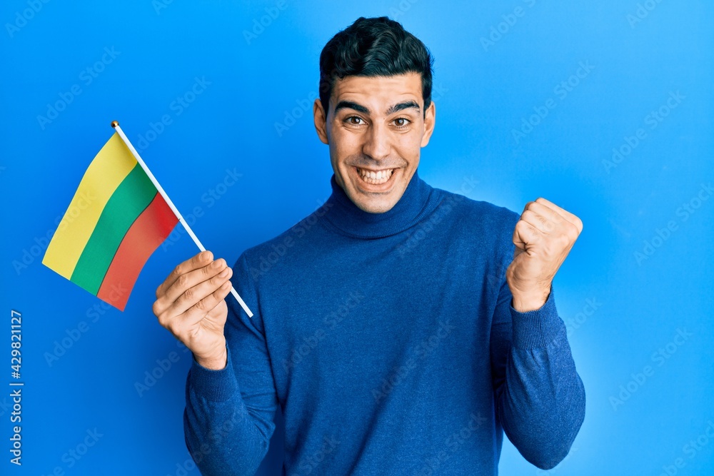 Handsome hispanic man holding lithuania flag screaming proud, celebrating victory and success very excited with raised arm Handsome hispanic man holding lithuania flag screaming proud, celebrating victory and success very excited with raised arm