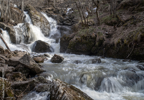 Waterfall in Bashkortostan in early spring. A stormy stream of water among large stones.
