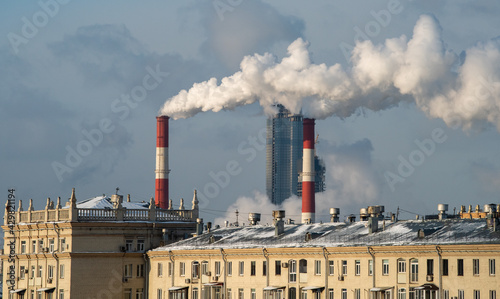 Smoke from the chimneys of a combined heat and power plant against the backdrop of a skyscraper under construction on a frosty winter day.