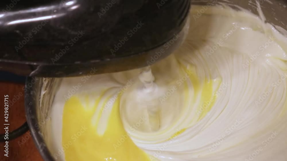 bright yellow egg mixing into batter in silver bowl