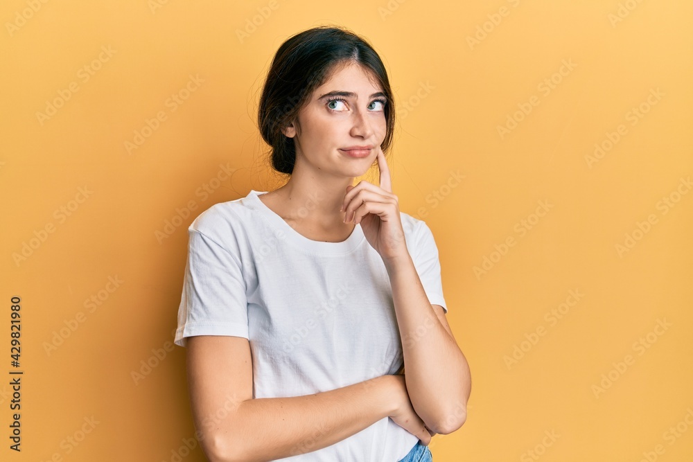 Young caucasian woman wearing casual white t shirt serious face thinking about question with hand on chin, thoughtful about confusing idea Young caucasian woman wearing casual white t shirt serious face thinking about question with hand on chin, thoughtful about confusing idea