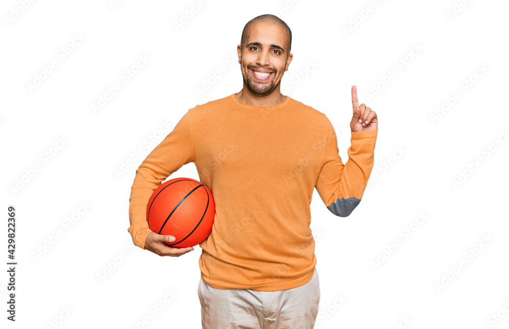 Hispanic adult man holding basketball ball surprised with an idea or question pointing finger with happy face, number one Hispanic adult man holding basketball ball surprised with an idea or question pointing finger with happy face, number one