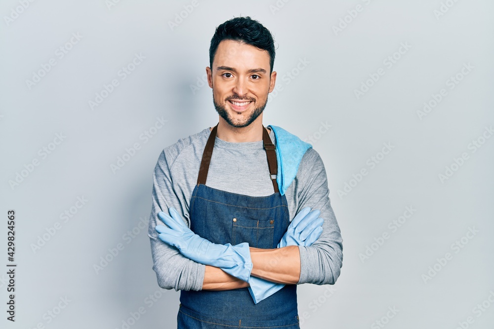 Young hispanic man wearing apron with arms crossed smiling with a happy and cool smile on face. showing teeth.