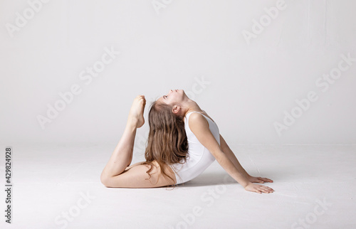 preteen girl gymnast trains on white background in white leotard. children's professional sports. rhythmic gymnastics.