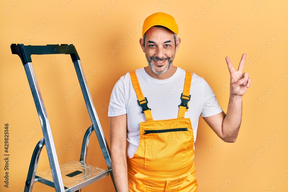 Handsome middle age man with grey hair holding ladder showing and pointing up with fingers number two while smiling confident and happy. Handsome middle age man with grey hair holding ladder showing and pointing up with fingers number two while smiling confident and happy.