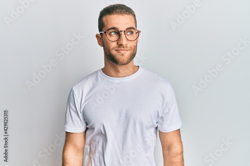 Young caucasian man wearing casual clothes and glasses smiling looking to the side and staring away thinking.