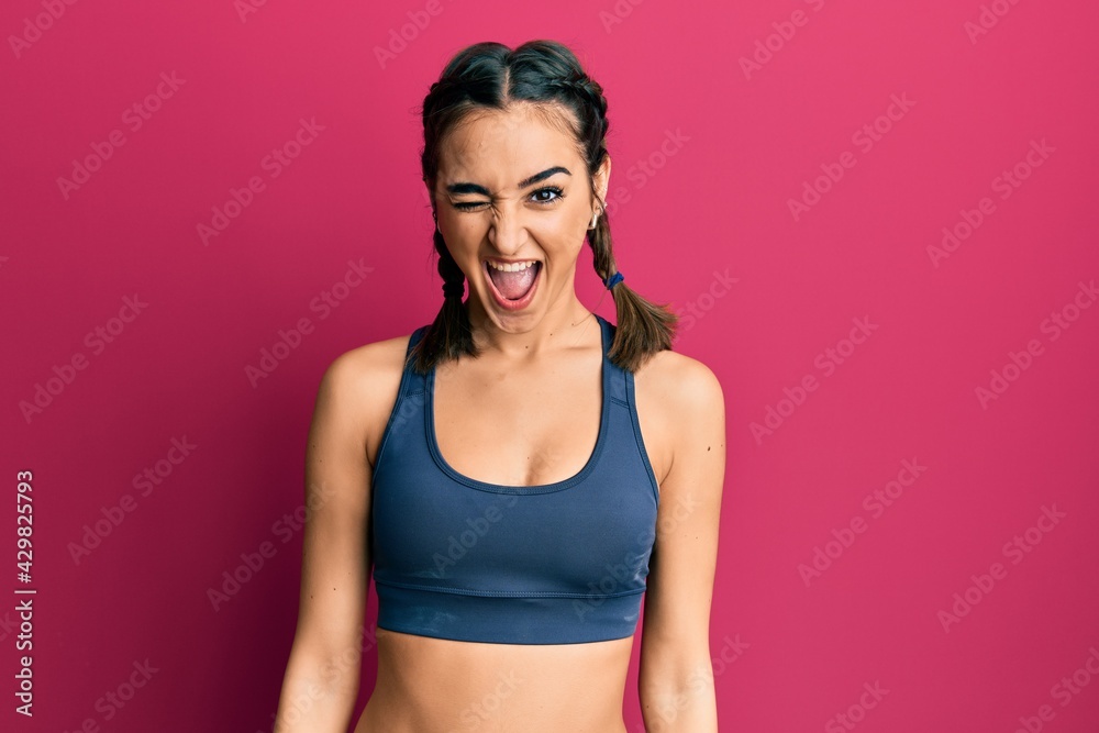 Young brunette girl wearing sportswear and braids winking looking at the camera with sexy expression, cheerful and happy face. Young brunette girl wearing sportswear and braids winking looking at the camera with sexy expression, cheerful and happy face.