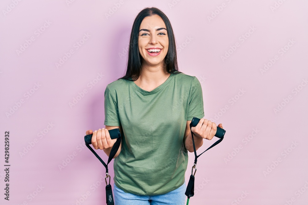 Beautiful woman with blue eyes training arm resistance with elastic arm bands smiling and laughing hard out loud because funny crazy joke.