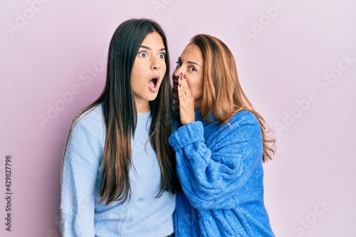 Hispanic family of mother and daughter wearing wool winter sweater hand on mouth telling secret rumor, whispering malicious talk conversation