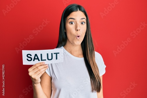 Young brunette woman holding salut french greeting scared and amazed with open mouth for surprise, disbelief face