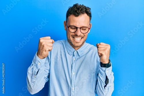 Young hispanic man wearing casual clothes and glasses excited for success with arms raised and eyes closed celebrating victory smiling. winner concept.