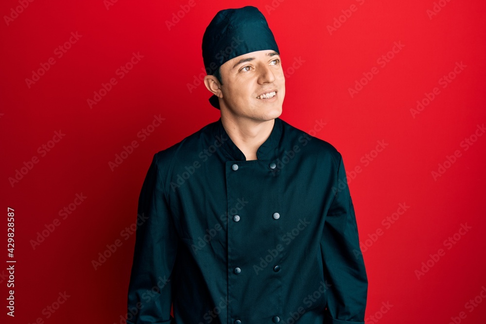 Handsome young man wearing professional cook uniform and hat looking away to side with smile on face, natural expression. laughing confident. Handsome young man wearing professional cook uniform and hat looking away to side with smile on face, natural expression. laughing confident.