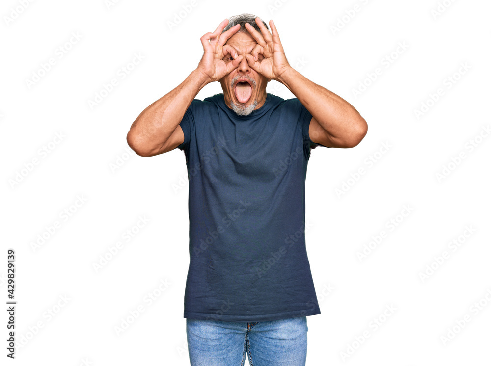 Middle age grey-haired man wearing casual clothes doing ok gesture like binoculars sticking tongue out, eyes looking through fingers. crazy expression. Middle age grey-haired man wearing casual clothes doing ok gesture like binoculars sticking tongue out, eyes looking through fingers. crazy expression.
