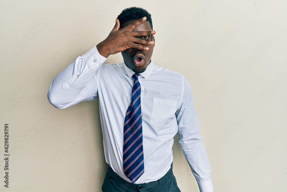 Handsome black man wearing glasses business shirt and tie peeking in shock covering face and eyes with hand, looking through fingers with embarrassed expression. Handsome black man wearing glasses business shirt and tie peeking in shock covering face and eyes with hand, looking through fingers with embarrassed expression.