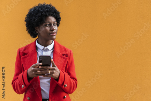 Happy smiling black woman using smart phone. Young African girl typing message with cell phone isolated on yellow background.Portrait of stylish African American girl using cell phone with copy space.